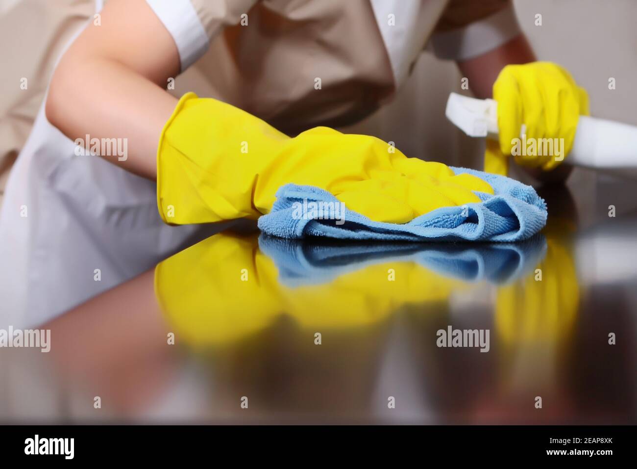 A uniformed maid is dusting the furniture. Cleaning in the hotel room. The person is unrecognizable. Out of focus. The concept of hotel business and cleaning. High-quality service in the hotel. Hands in protective gloves. Stock Photo