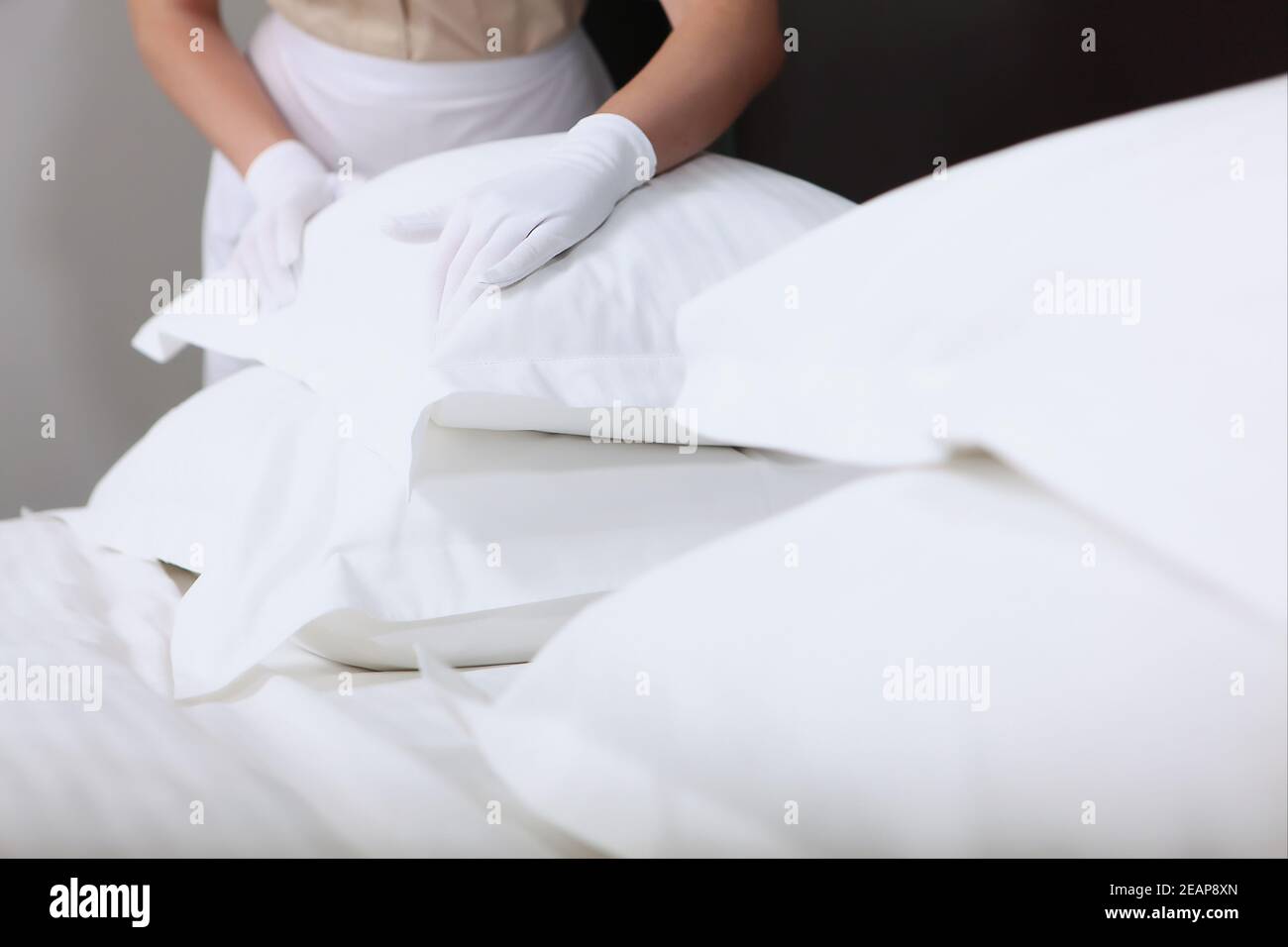 The maid changes the bed linen. Pillows are out of focus. Unrecognizable person. Hands in white cotton gloves. The concept of quality service in the hotel. Hotel business. Stock Photo