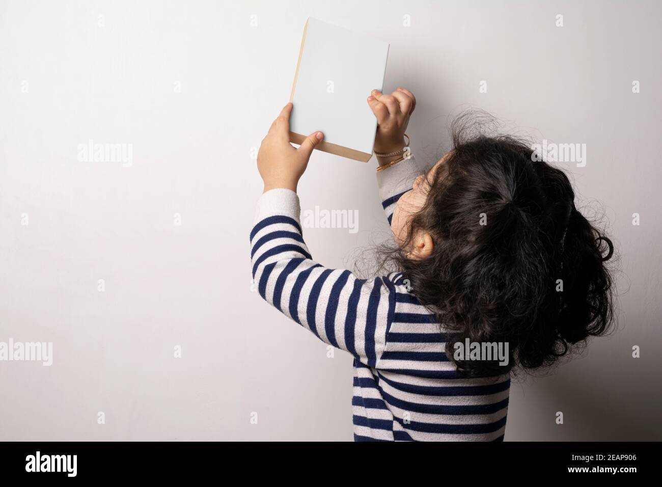 Little girl holding a novel book with blank cover in front white background mock-up series Stock Photo