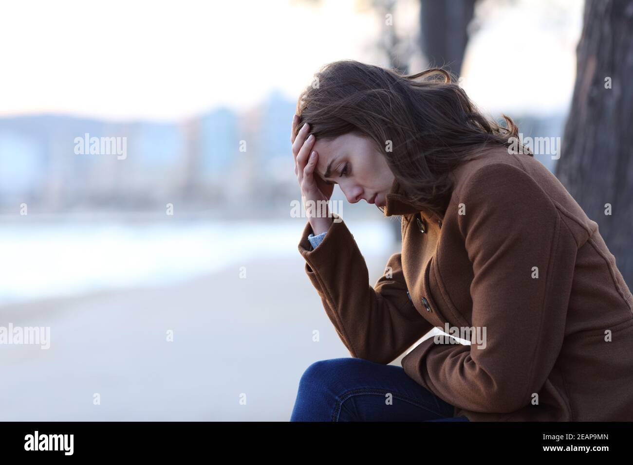 Sad woman complaining on a bench in winter on the beach Stock Photo