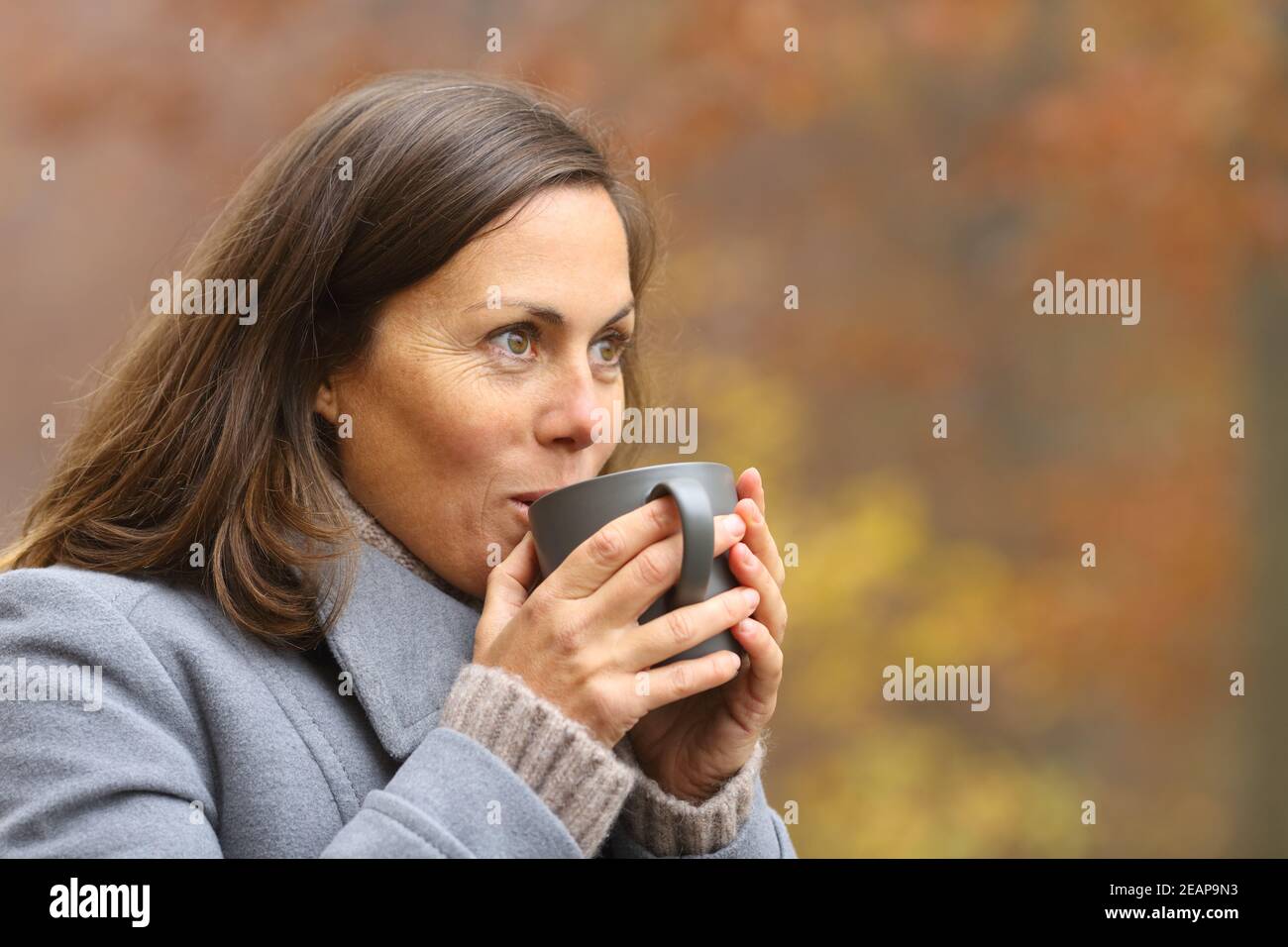 Adult woman drinking coffee in a park in autumn Stock Photo