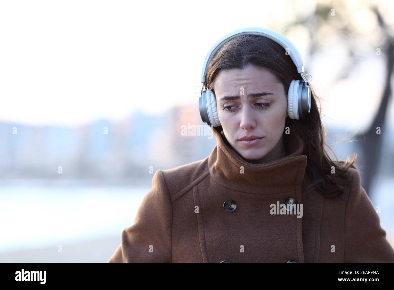 Sad woman walking listening to music alone in winter Stock Photo