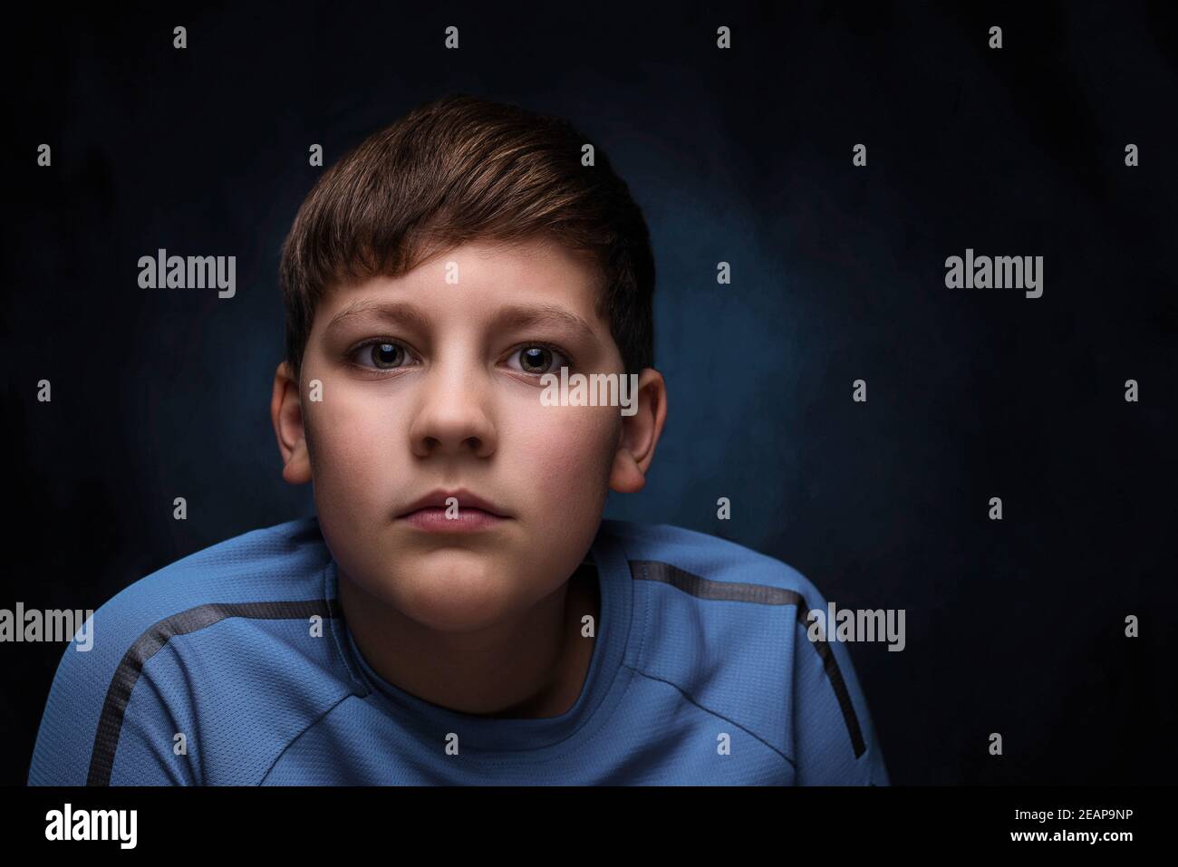 portrait of a serious european teenage boy with light brown hair, dressed in a light blue turquoise sports t-shirt, on an isolated background Stock Photo