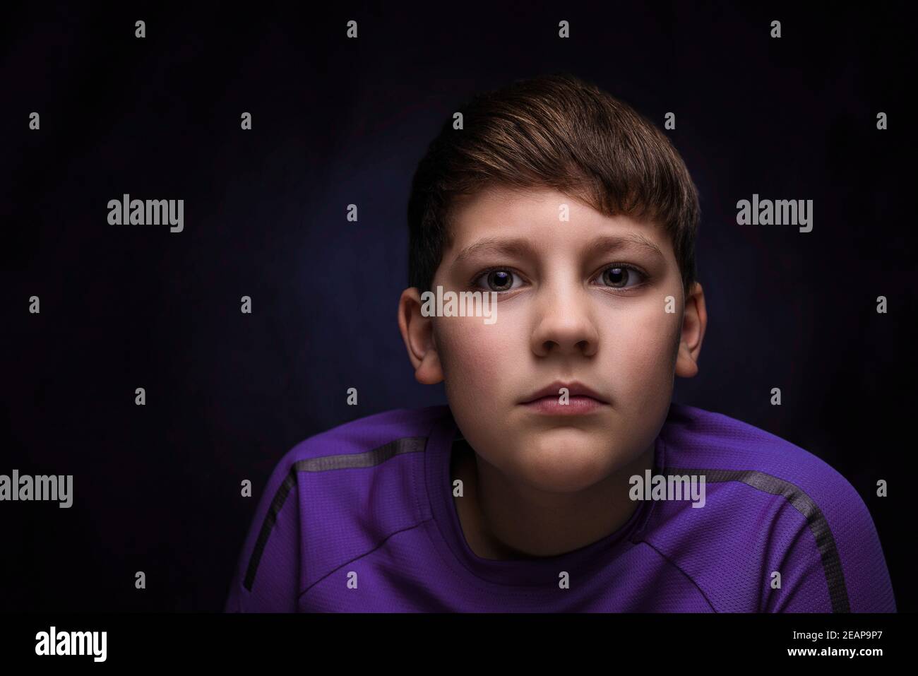 portrait of a handsome teenage boy with dark blonde hair and bangs wearing a sporty purple t-shirt on an isolated background Stock Photo