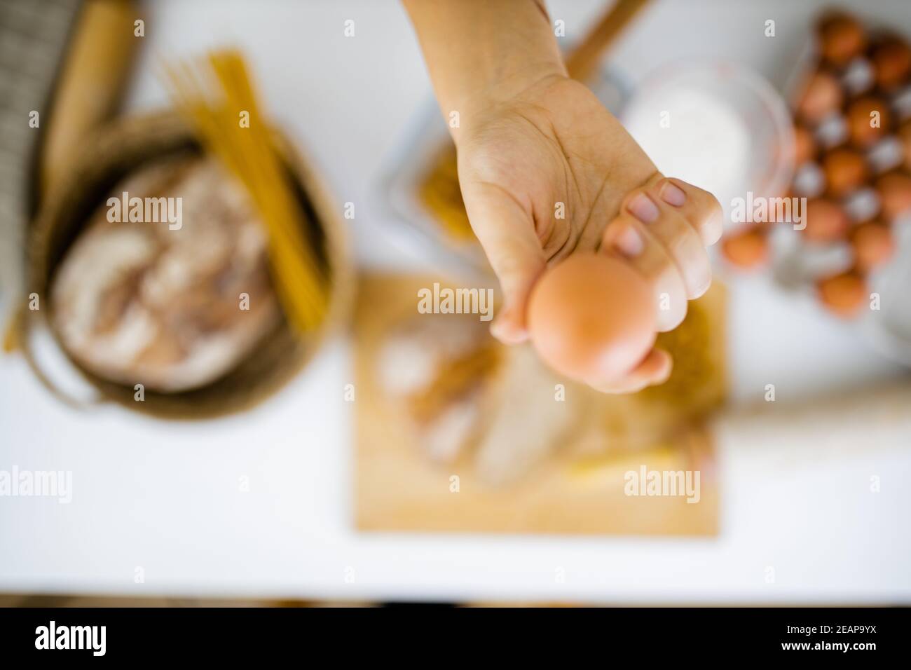 Female hand holding an egg above ingredients on a table Stock Photo