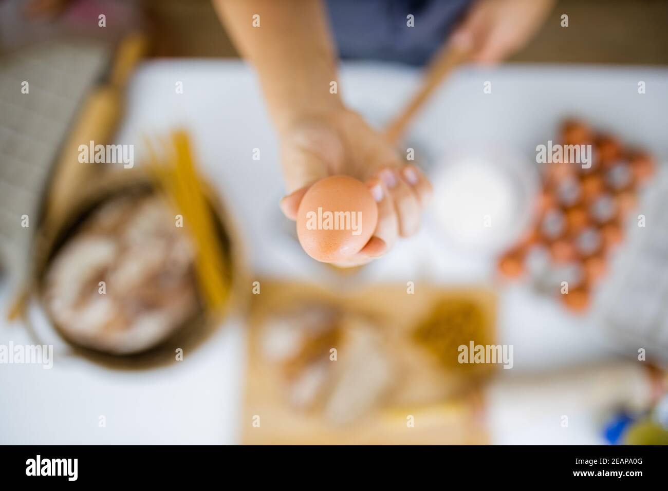 Female hand holding an egg above ingredients on a table Stock Photo