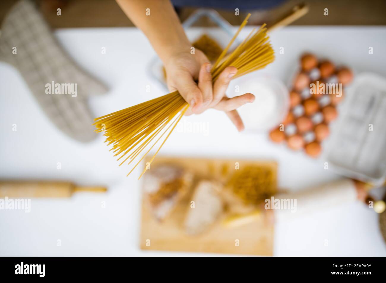 Female hand holding uncooked spaghetti above ingredients on a table Stock Photo