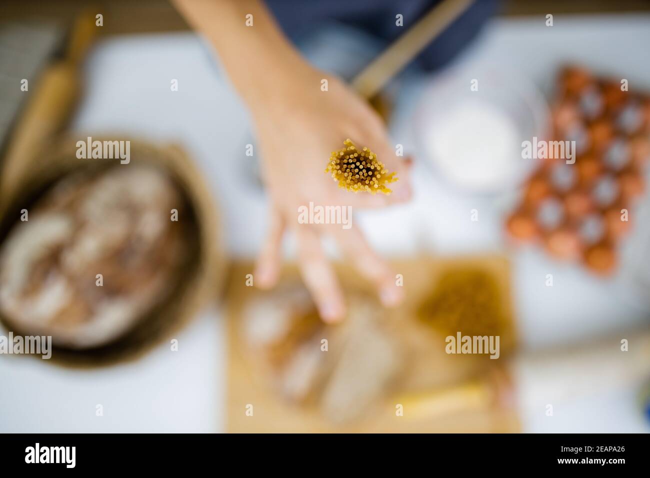 Female hand holding uncooked spaghetti above ingredients on a table Stock Photo