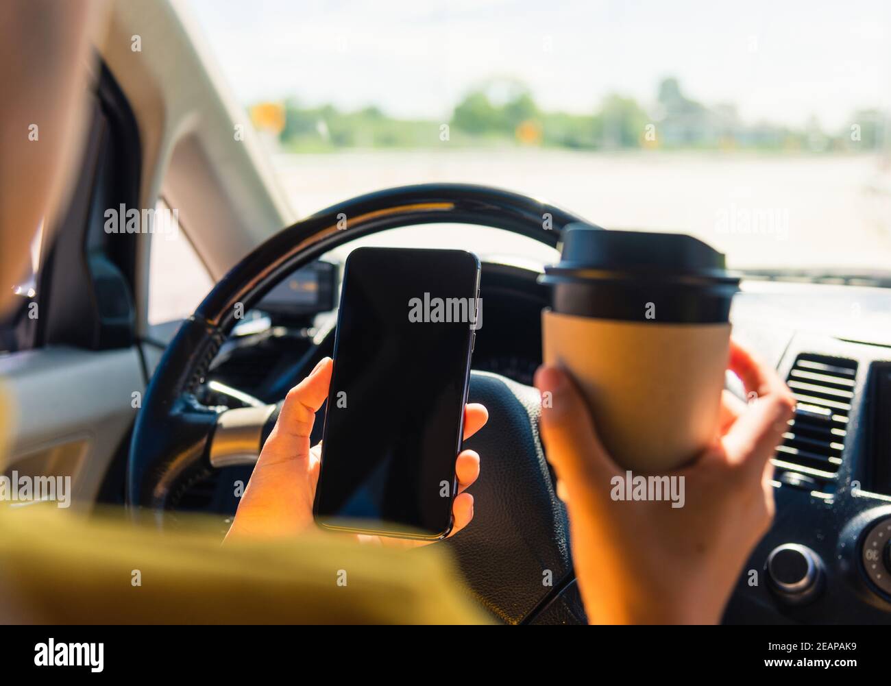 woman drinking hot coffee takeaway cup inside a car and using smartphone Stock Photo