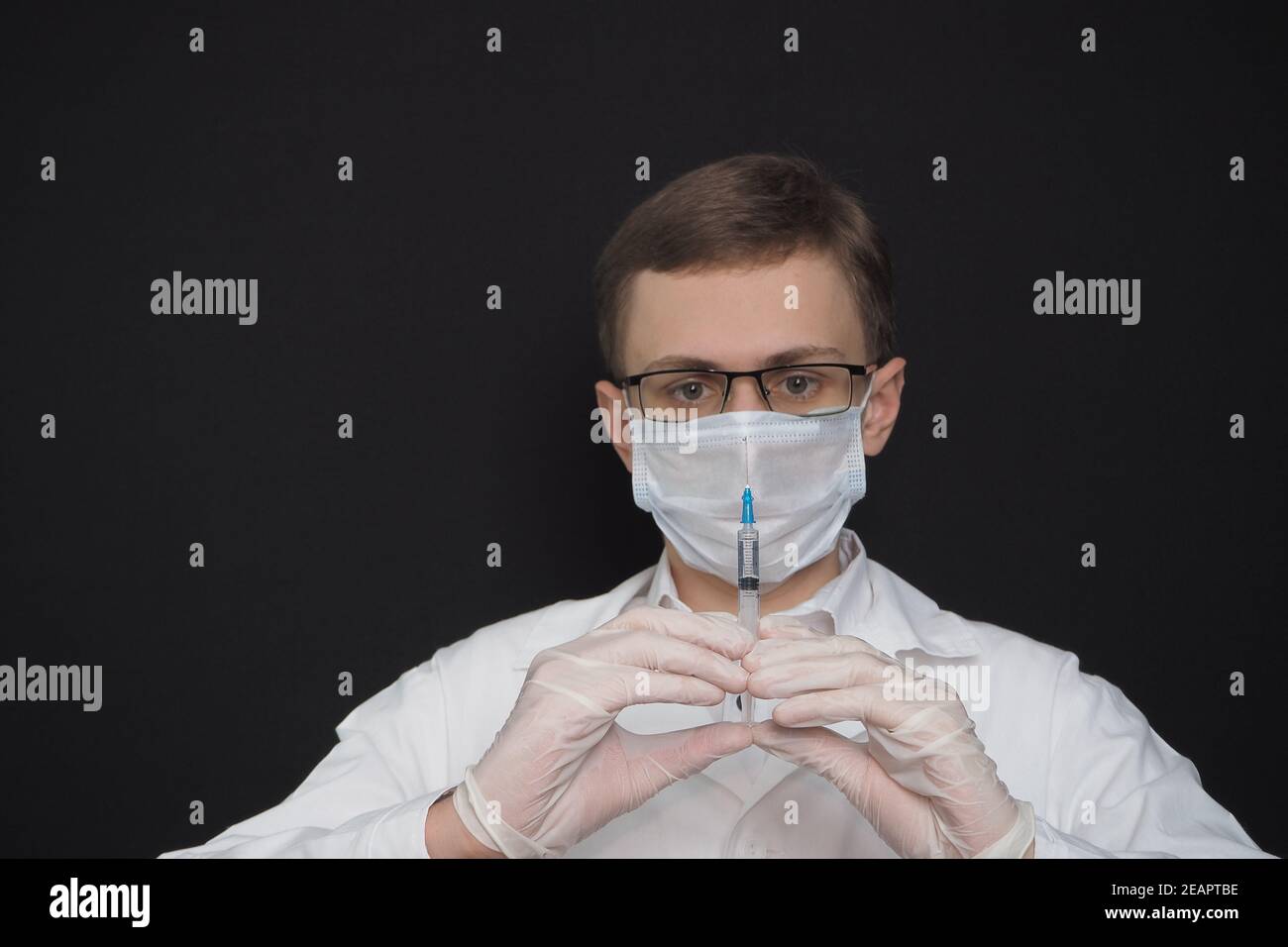 Science and Medicine, Young doctor in medical mask, glasses, rubber gloves and with a syringe in his hands. Stock Photo