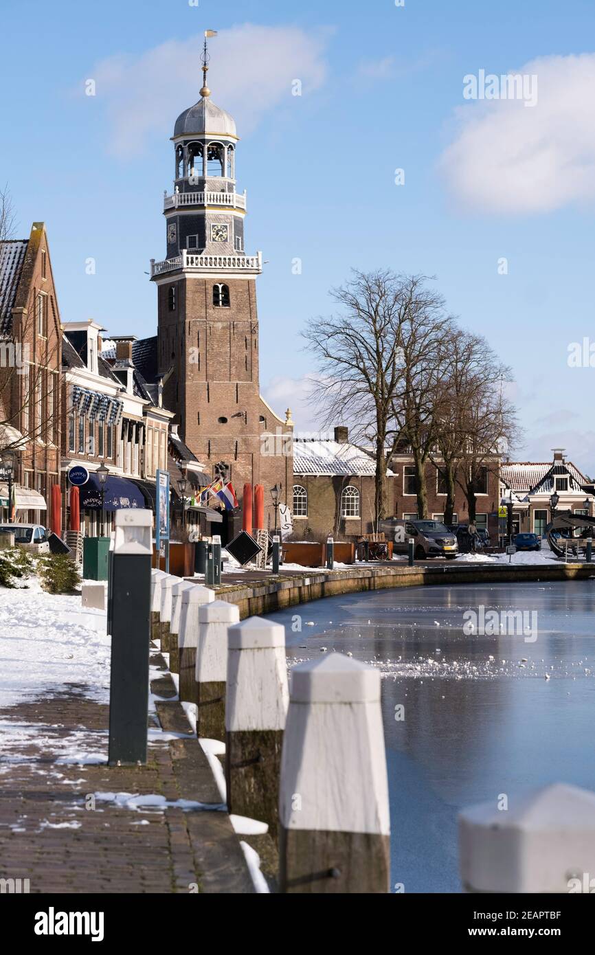 Winter Cityscape of Lemmer, the Netherlands with Reformed Church and shops on the quay and ice in Het Dok, blue sky and sun Stock Photo