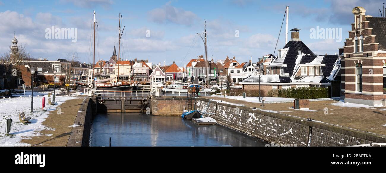 Cityscape of Lemmer, the Netherlands, harbor in winter with snow in Friesland with an almost empty lock in front with a boat frozen in ice. Widescreen Stock Photo
