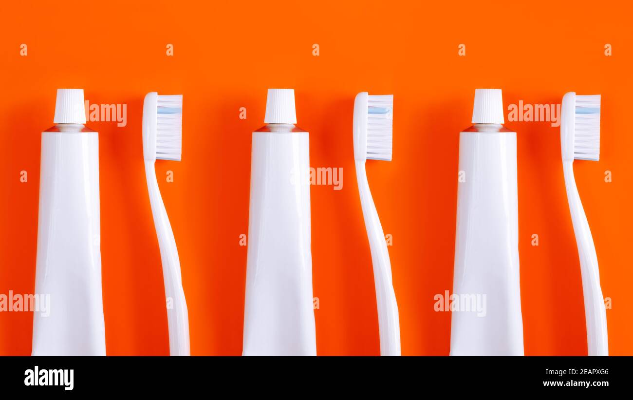 Dental hygiene objects: toothbrush and toothpaste. White generic accessories for keeping teeth health in bright orange backdrop, product photography Stock Photo
