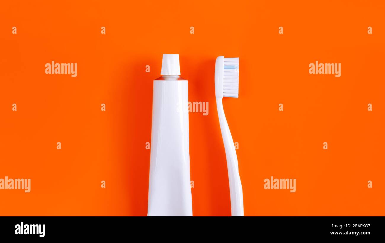 Dental hygiene objects: toothbrush and toothpaste. White generic accessories for keeping teeth health in bright orange backdrop, product photography Stock Photo