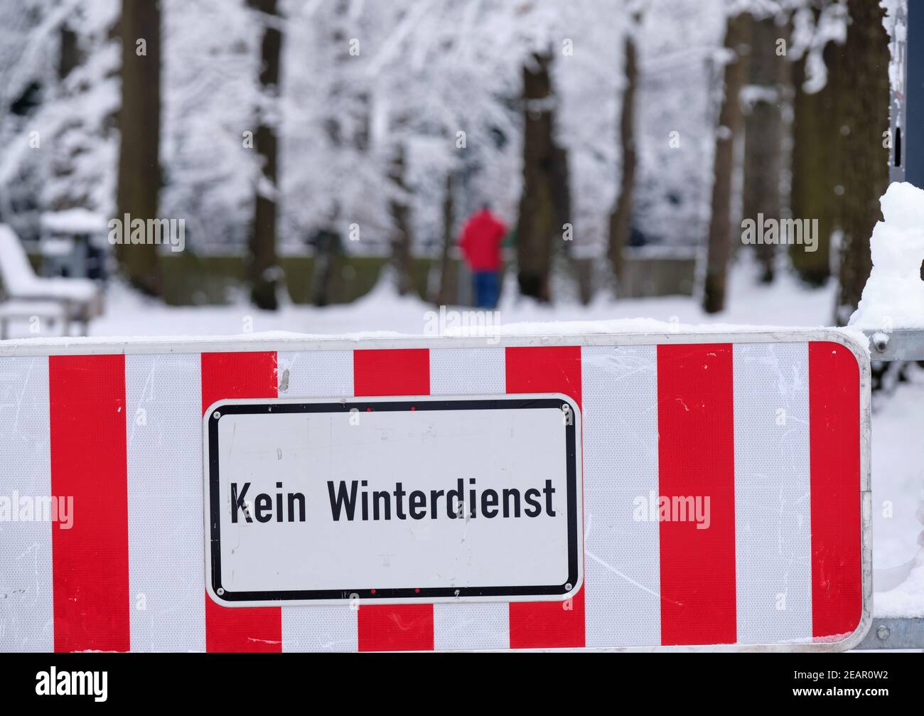 A red and white sign on a footpath at the entrance of a park informs about Kein Winterdienst  (in English: no winter maintenance). Seen in  Bavaria in Stock Photo