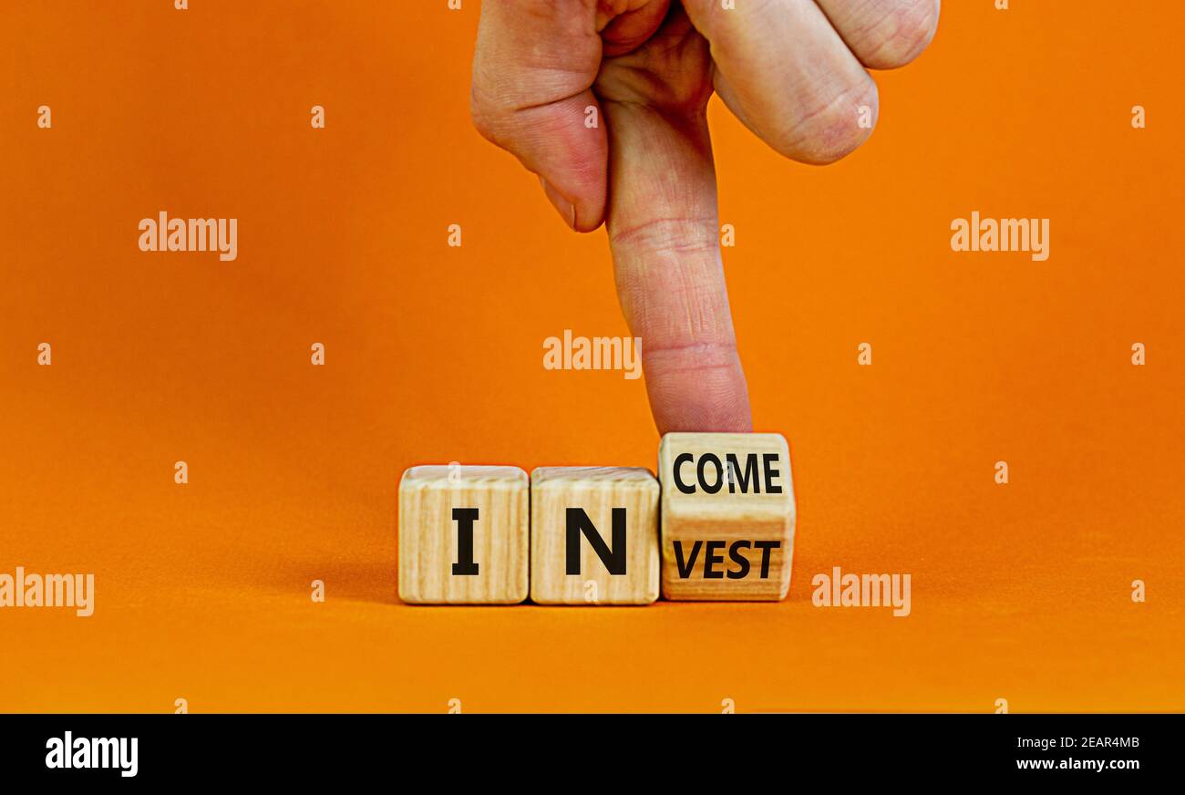 Invest or income symbol. Businessman turns a wooden cube and changes the word 'invest' to 'income'. Beautiful orange background, copy space. Business Stock Photo