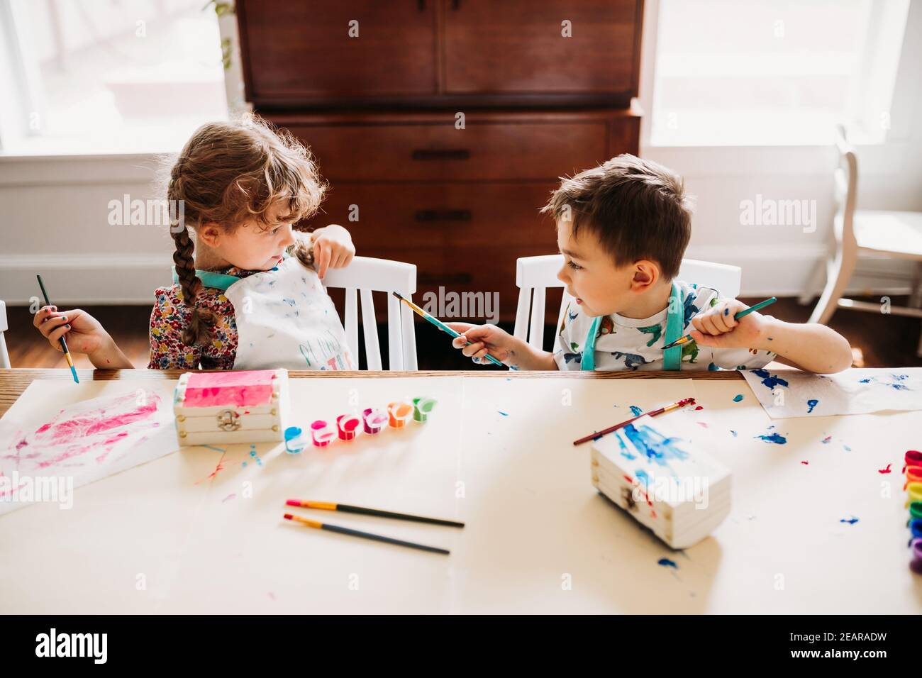 Brother and sister sitting at table painting with rainbow paints Stock Photo