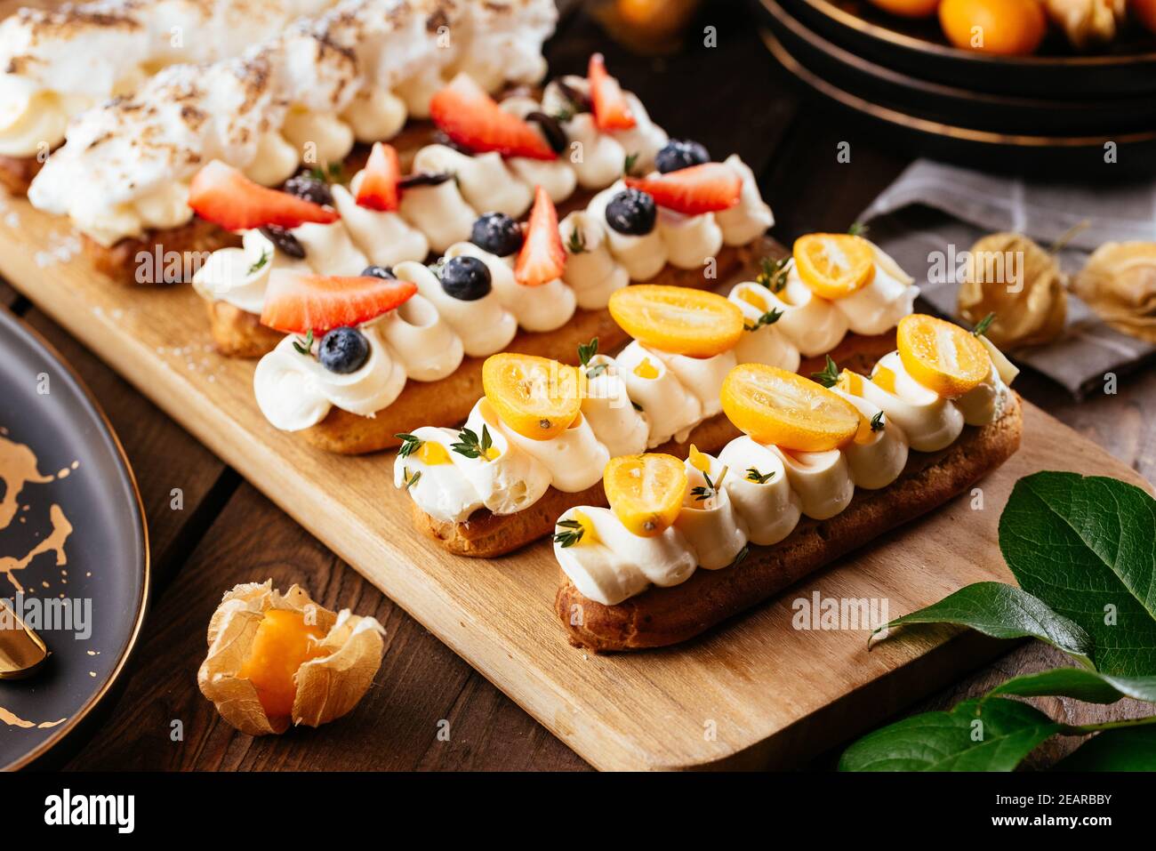Freshly baked delicious eclairs with berries on a wooden olive board Stock Photo