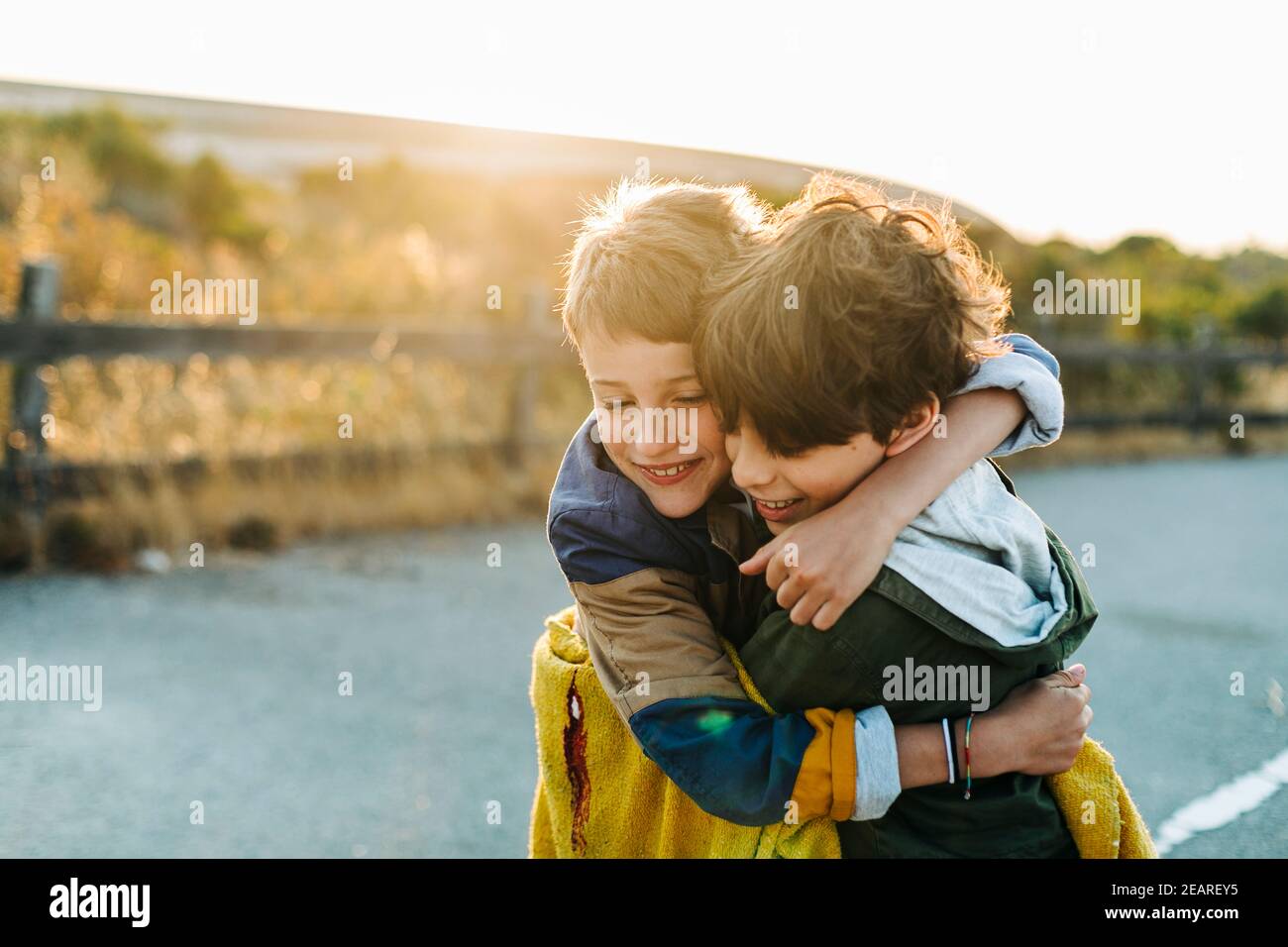 Back flare light over tweens brothers hugging in road park at sunrise Stock Photo