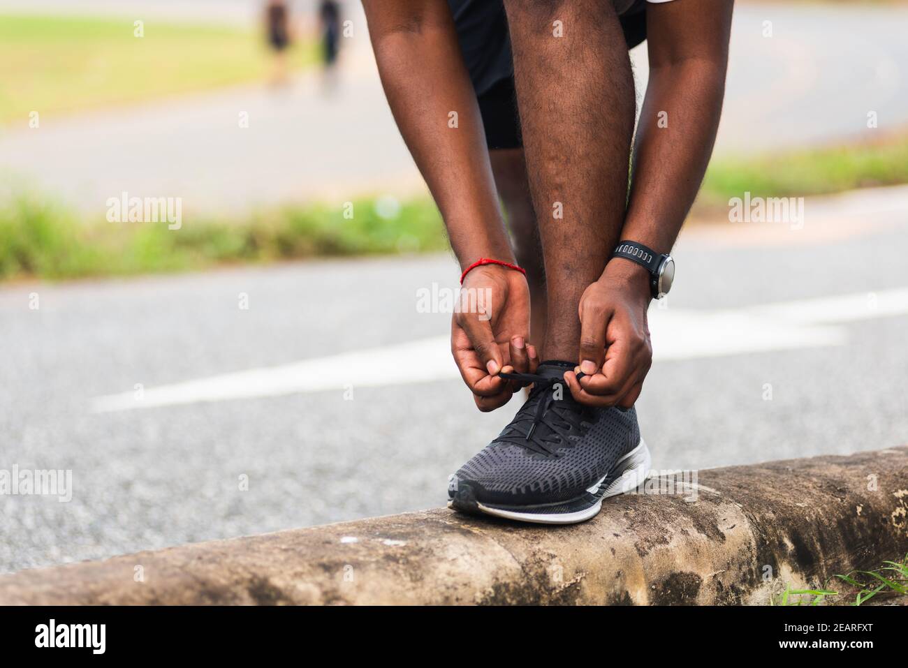 runner black man wear watch stand step on the footpath trying shoelace running shoes Stock Photo