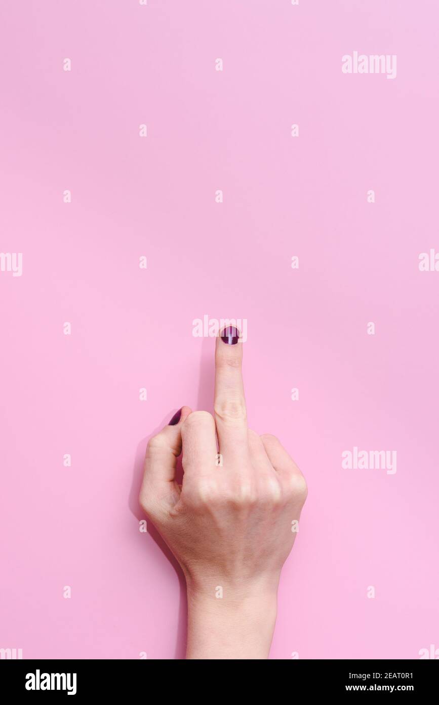 vertical studio take of the hand of a caucasian female raising middle finder showing an offensive gesture on a pink background. Concept of women disco Stock Photo