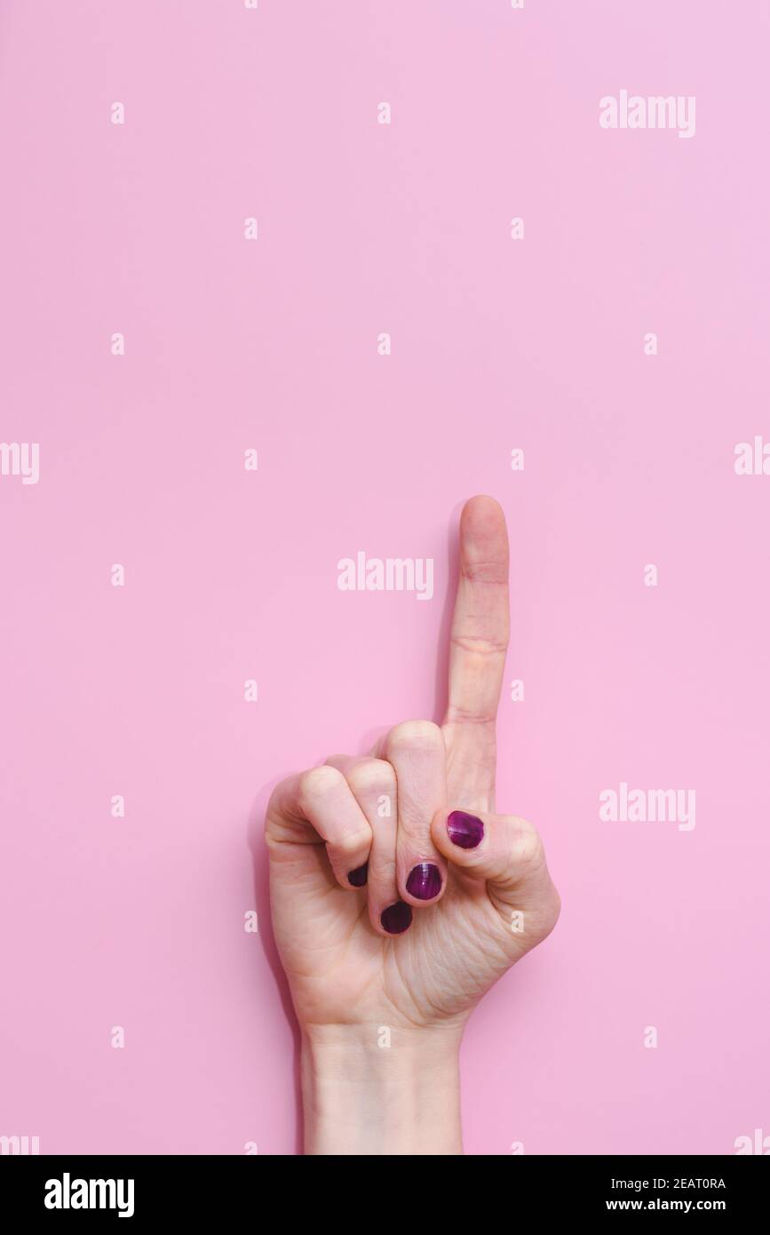 vertical take of a hand of a caucasian woman raising the index finger on a pink background. Concept of asking a turn to speak or to do questions Stock Photo
