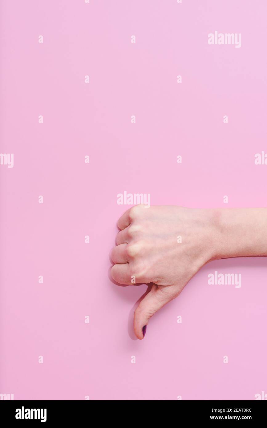 vertical take of the hand of a caucasian woman doing gesture of thumbs down on a pink background. Concept of disagreement and negativeness Stock Photo