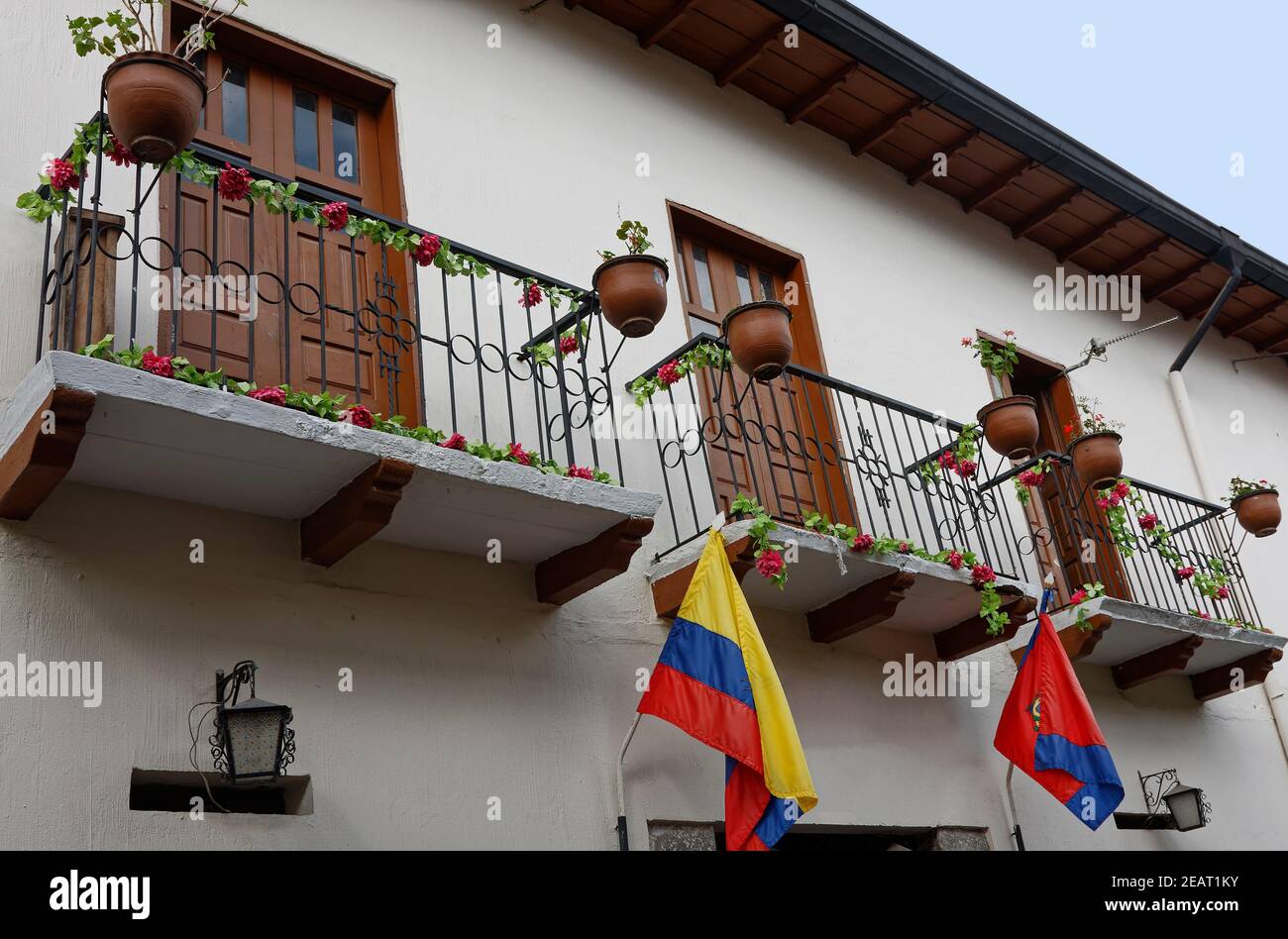 3 balconies, old white building, 2 flags, doors, flower garlands, pots on railings, wrought iron light fixtures, South America, Ronda District, Quito, Stock Photo