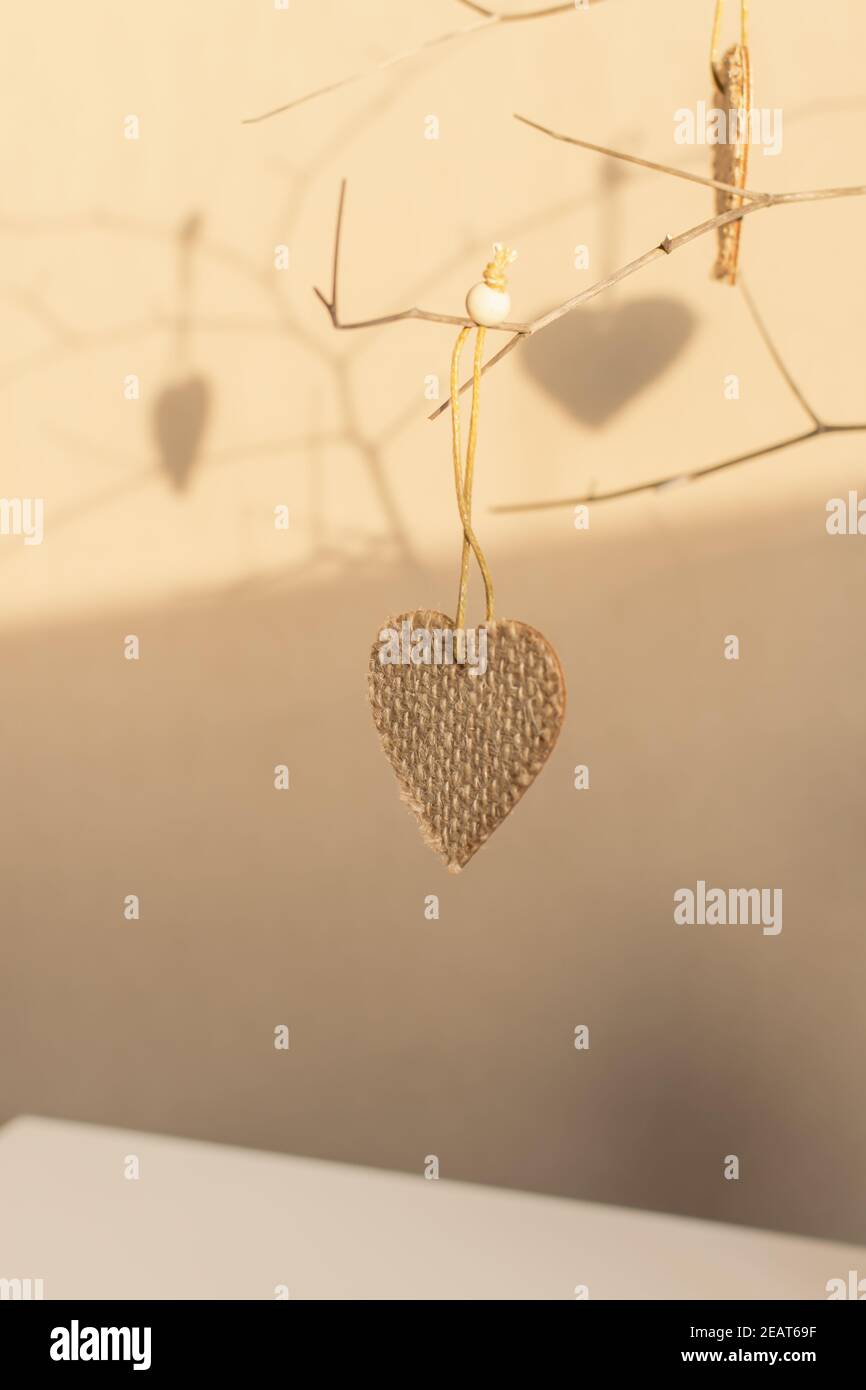 Creative composition in neutral colors for Valentine's Day. Hearts on a branch in a vase on the table. Handmade, coarse burlap fabric. Warm home atmos Stock Photo