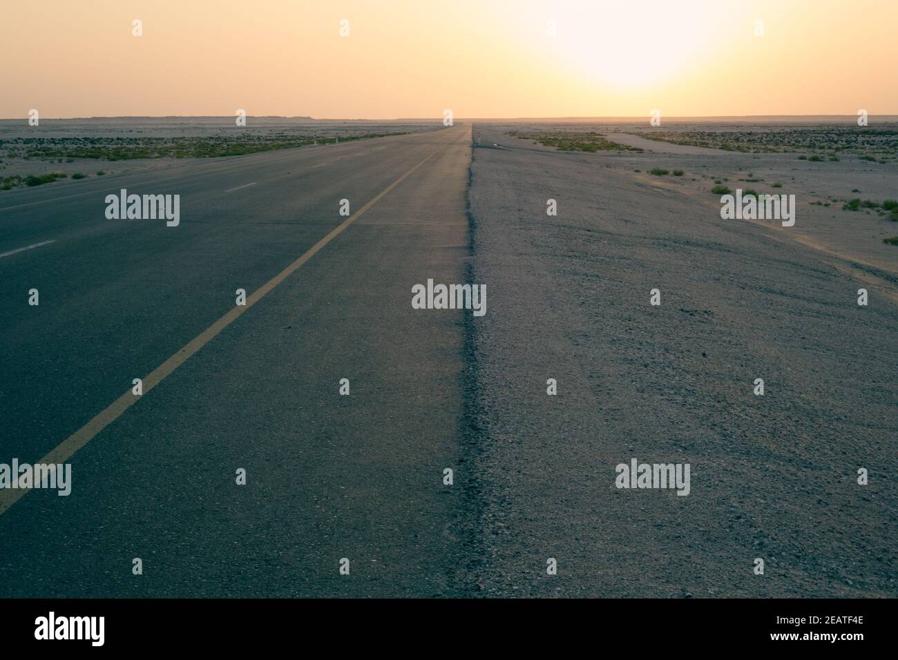 Empty single lane highway through flat desert at sunrise Stock Photo