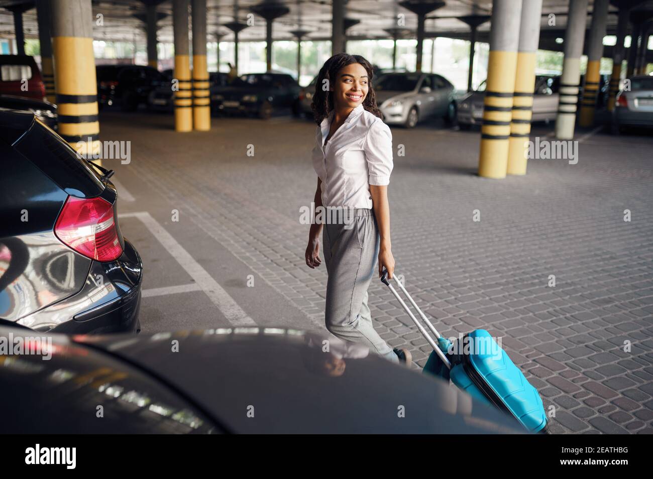 Young woman with suitcase in car parking Stock Photo