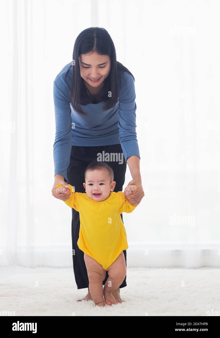 baby taking first steps learning to walk with mother Stock Photo