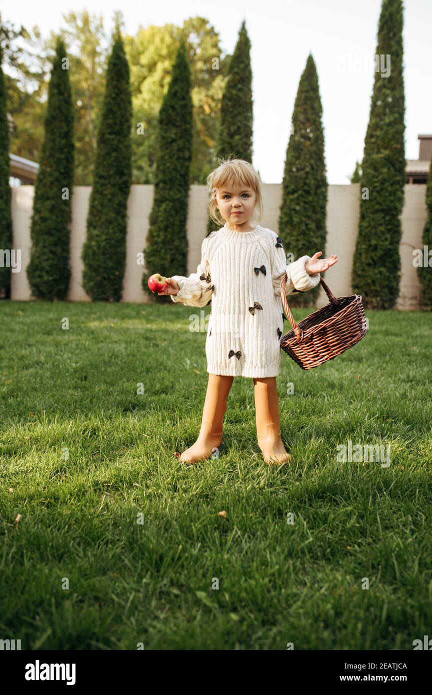 Little girl with basket eats an apple in garden Stock Photo