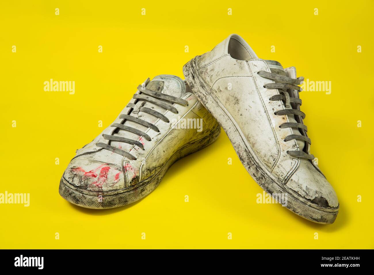 Dirty shoes, vintage white torn sneakers isolated on a yellow