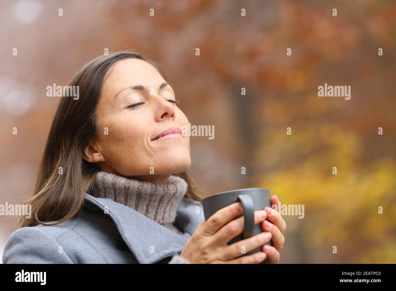Relaxed adult woman holding coffee cup breathing in autumn Stock Photo