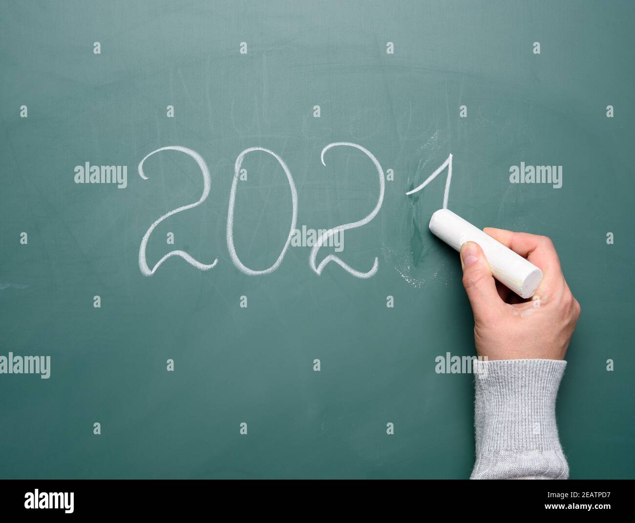female hand holds a piece of white chalk and writes on a green school board 2021 Stock Photo
