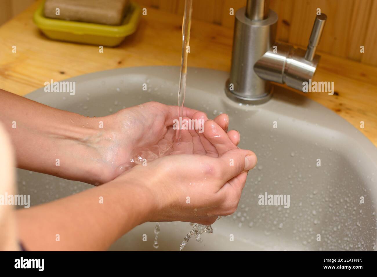 In the palm of the girl pouring water from the tap in the sink Stock Photo