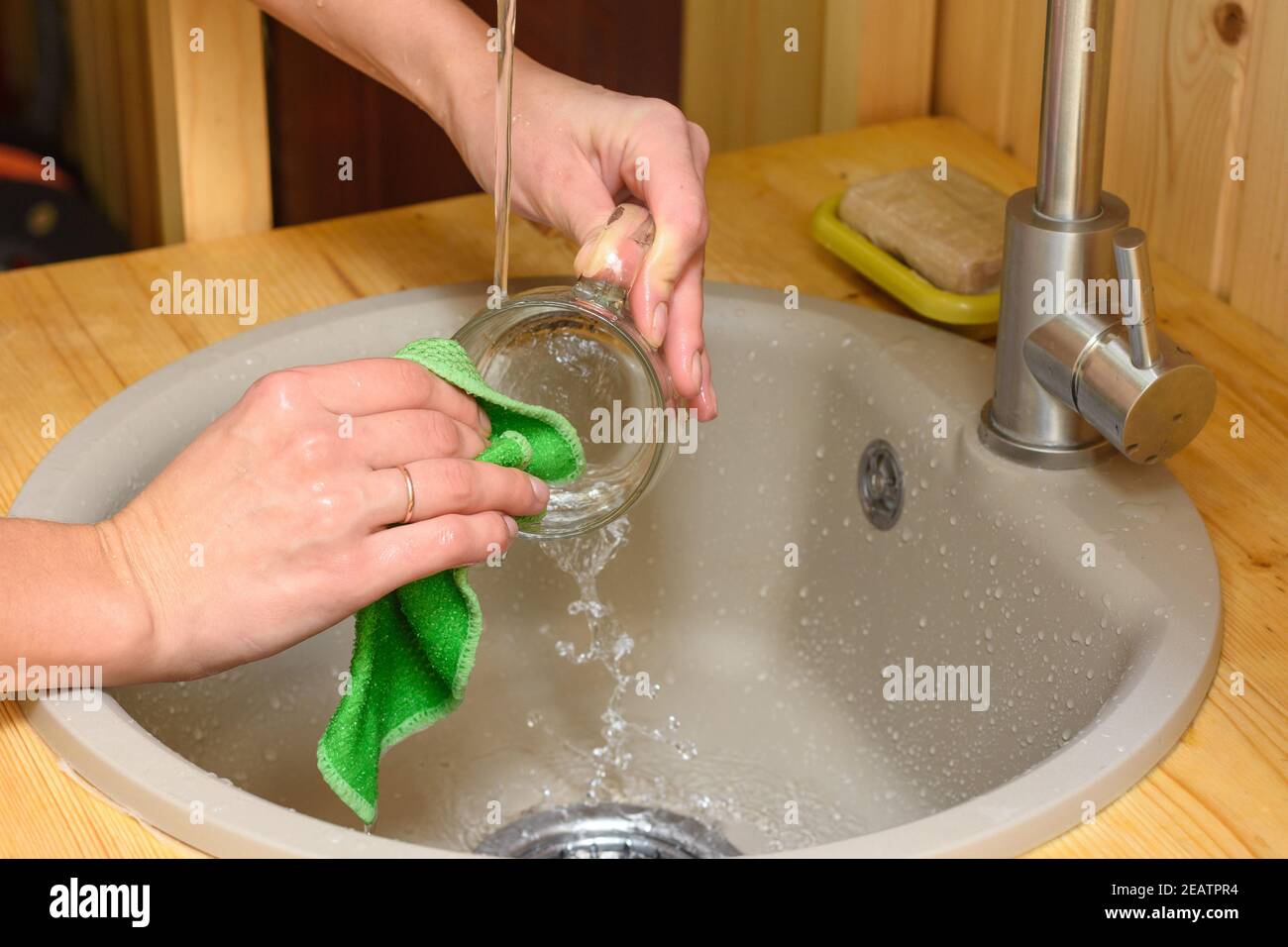 Girl's hands washing dishes in a kitchen with a wooden countertop Stock Photo