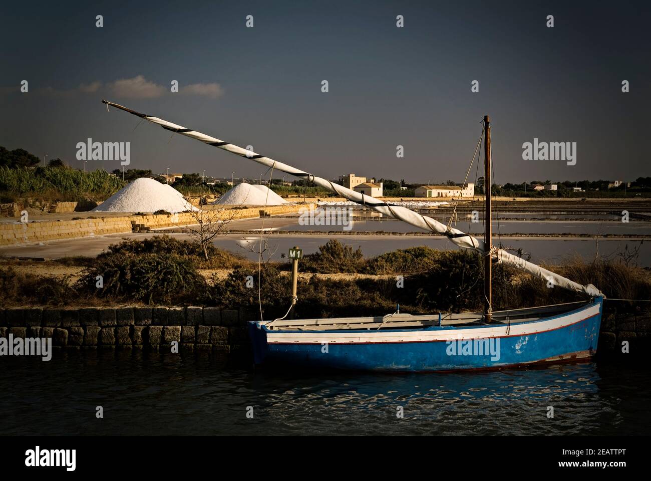A boat is docked next to a body of water, salt pans in Marsala, Sicily Stock Photo