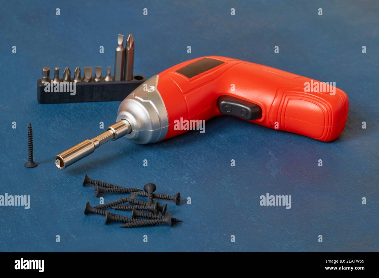 Electric cordless screwdriver with a set of bits, self-cutting screws, close-up on a blue background, shallow depth of sharpness Stock Photo