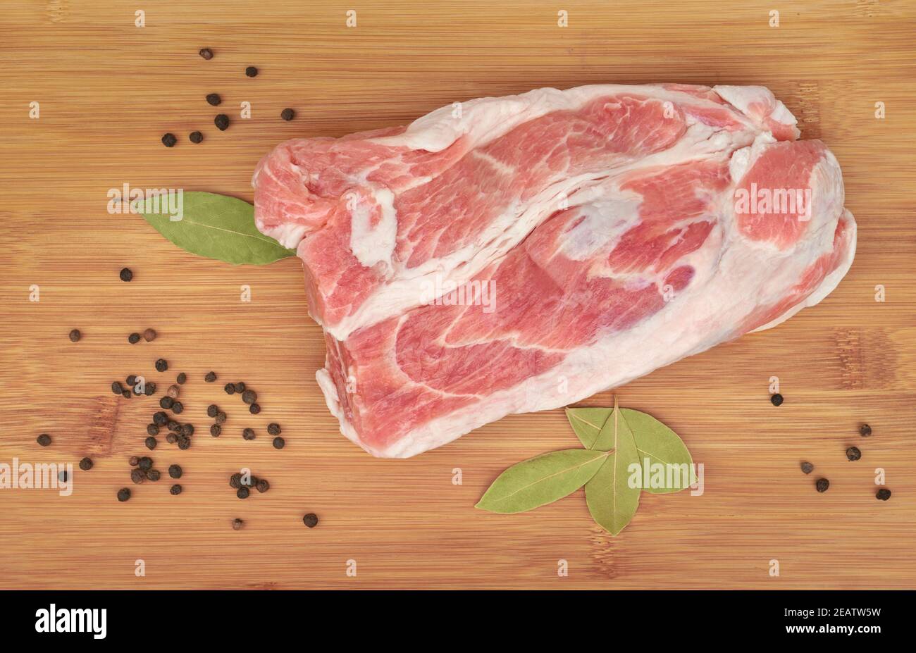 Photo of raw meat. Pork neck with pepper and bay leaf on a wooden board. View from above Stock Photo