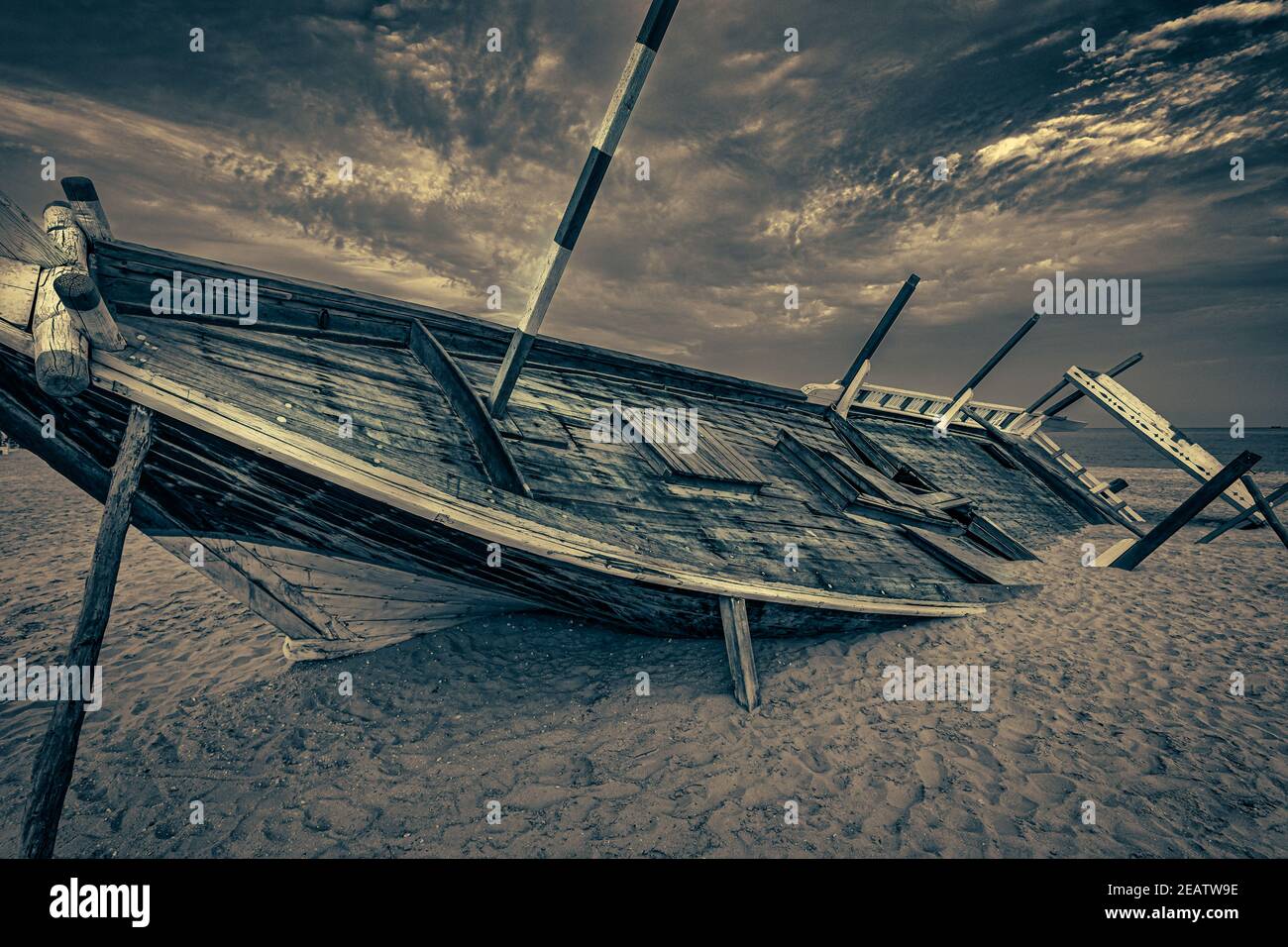 Old Arabic wooden boat (dhow) stranded on the beach black and white close up image with clouds in the sky Stock Photo