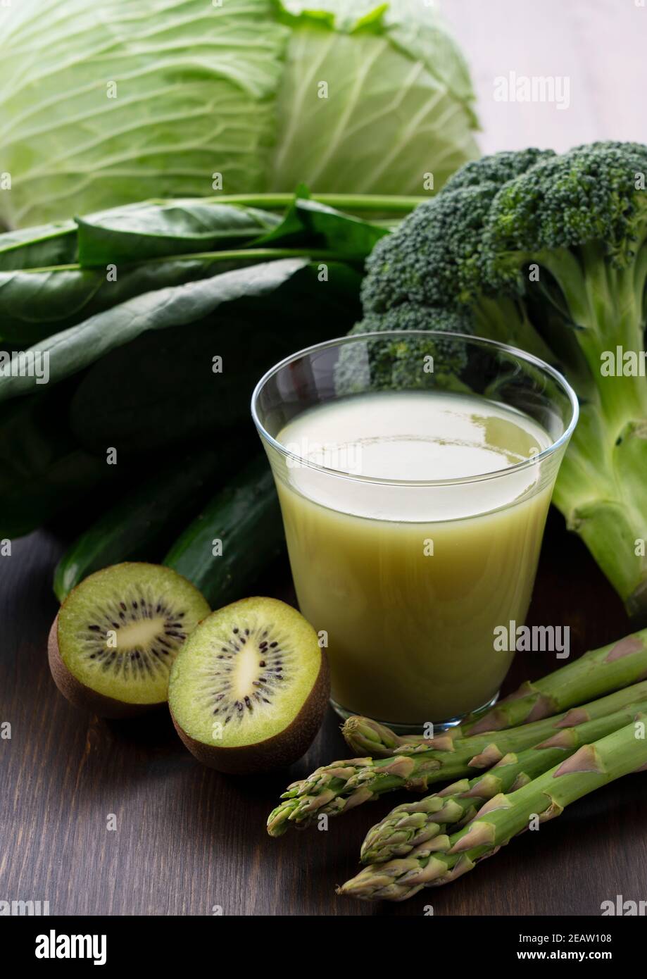 A lot of green vegetables placed on a wooden background and a glass of vegetable juice Stock Photo