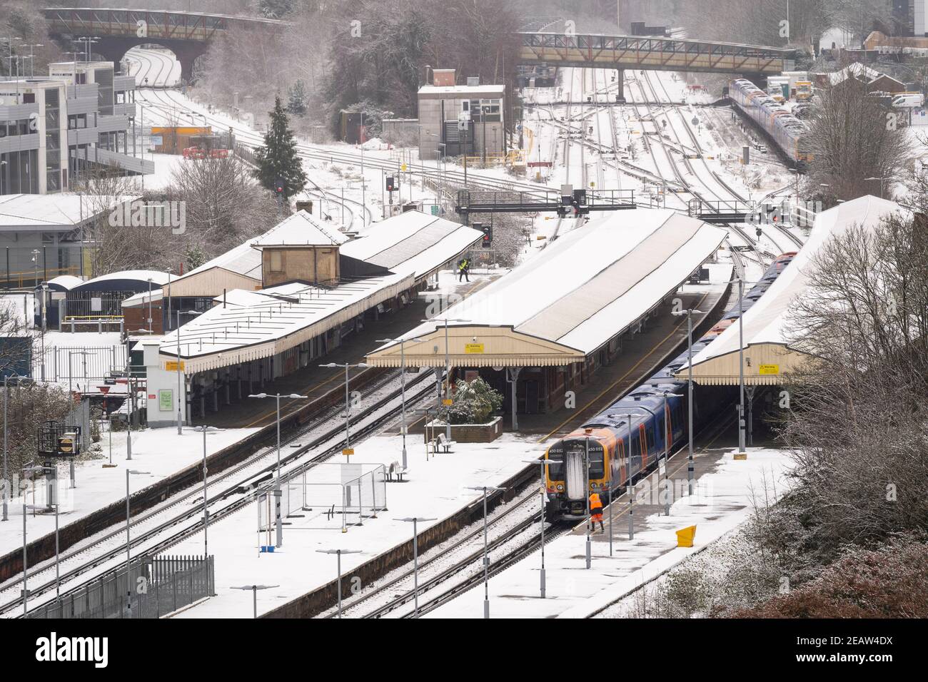 A railway worker clearing snow from a platform next to a South Western Railway train at Basingstoke railway station during January snowfall, 2021, UK Stock Photo