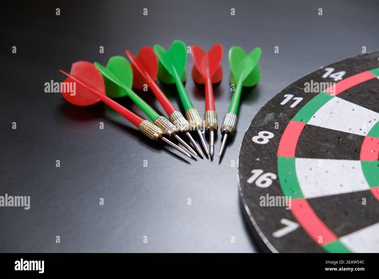dartboard and red, green and yellow darts on a black background Stock Photo