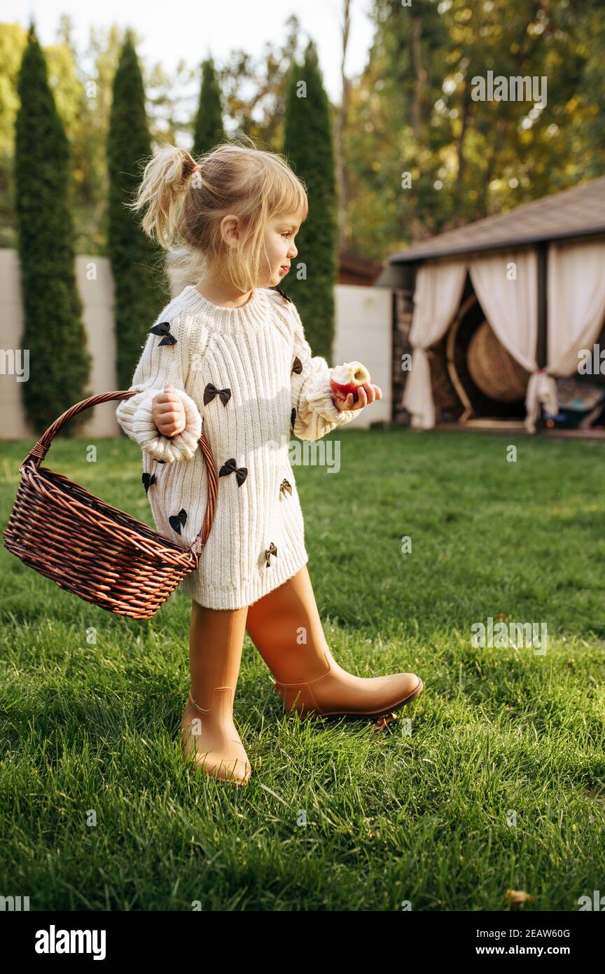 Little girl with basket eats an apple in garden Stock Photo