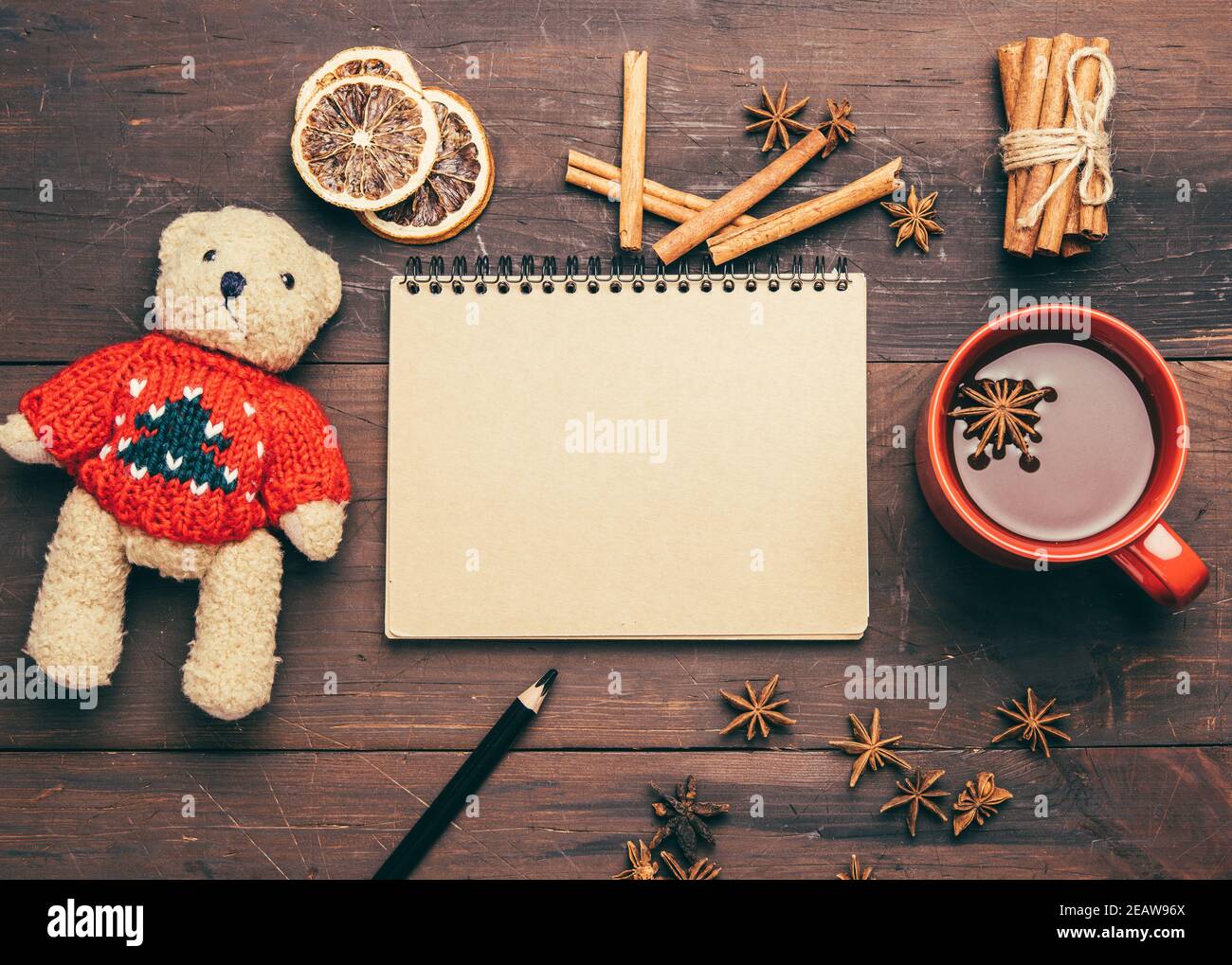 red ceramic cup with cocoa, notepad with blank sheets and brown teddy bear toy on a wooden table Stock Photo