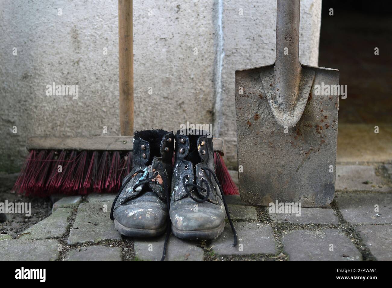 old worn painted work boots with a yard broom and a spade Stock Photo