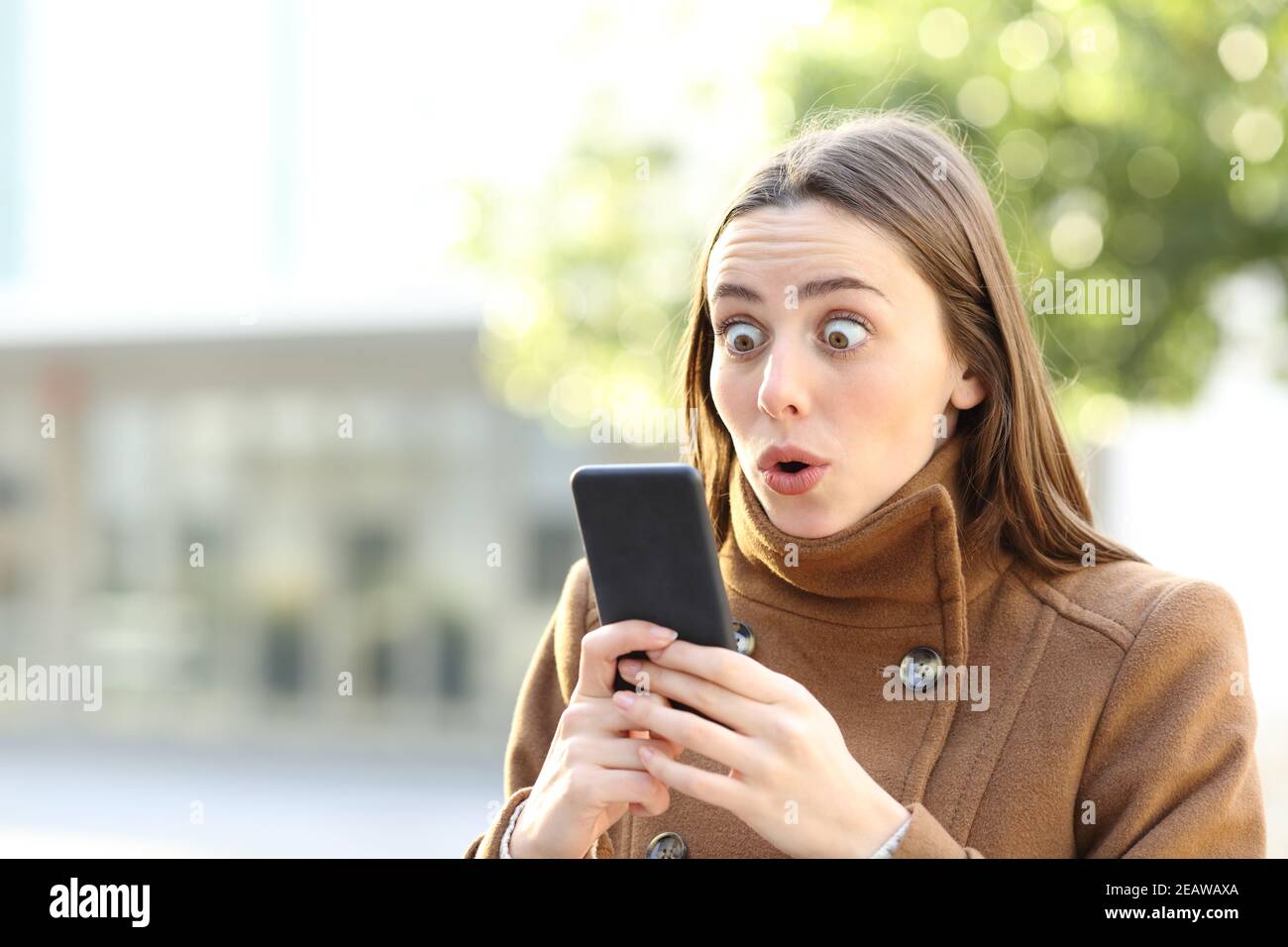 Amazed woman checking mobile phone in winter Stock Photo