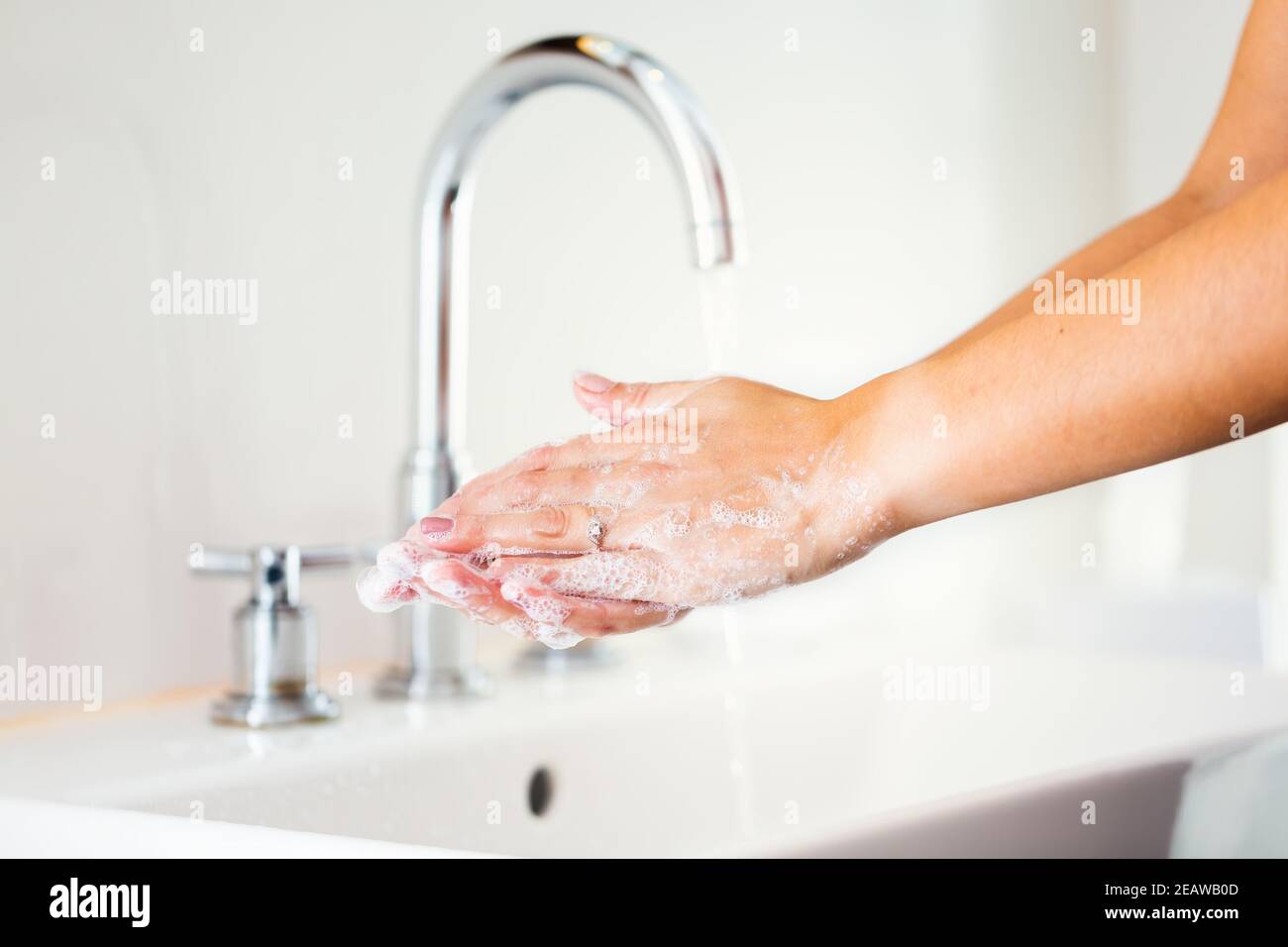 Woman washing hands with soap in bathroom with flowing water Stock